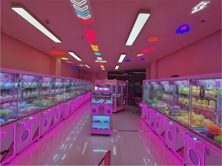 Long aisle of installed claw machines under pink neon lighting, showing high-capacity arcade layout and rows of plush-filled cabinets.