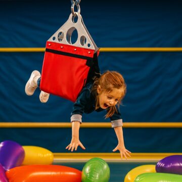 Girl hanging in a human claw harness reaching for colorful inflatable prizes.